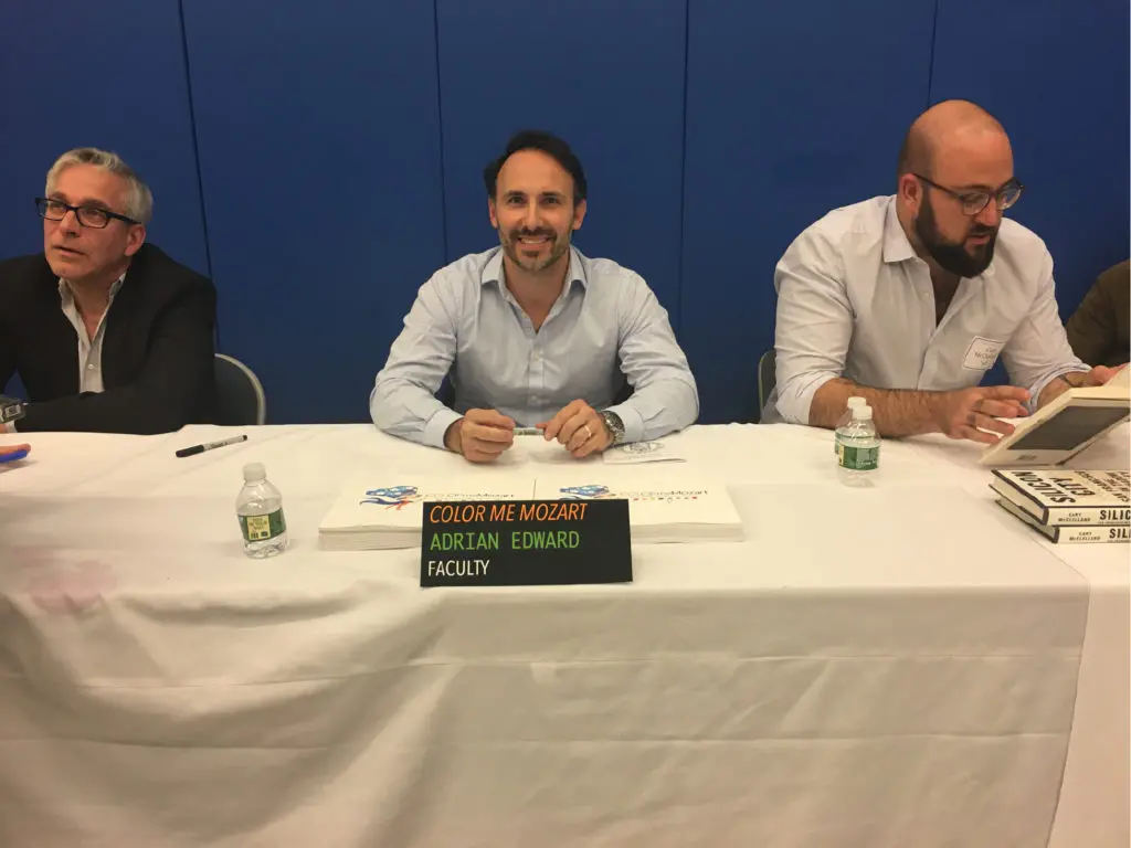 Three men sitting at a table with a sign