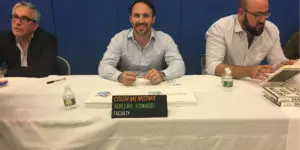 Three men sitting at a table with a sign