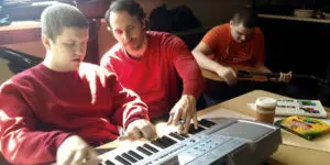 A man and two boys playing on an electronic keyboard.