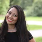 A woman smiling for the camera in front of some trees.