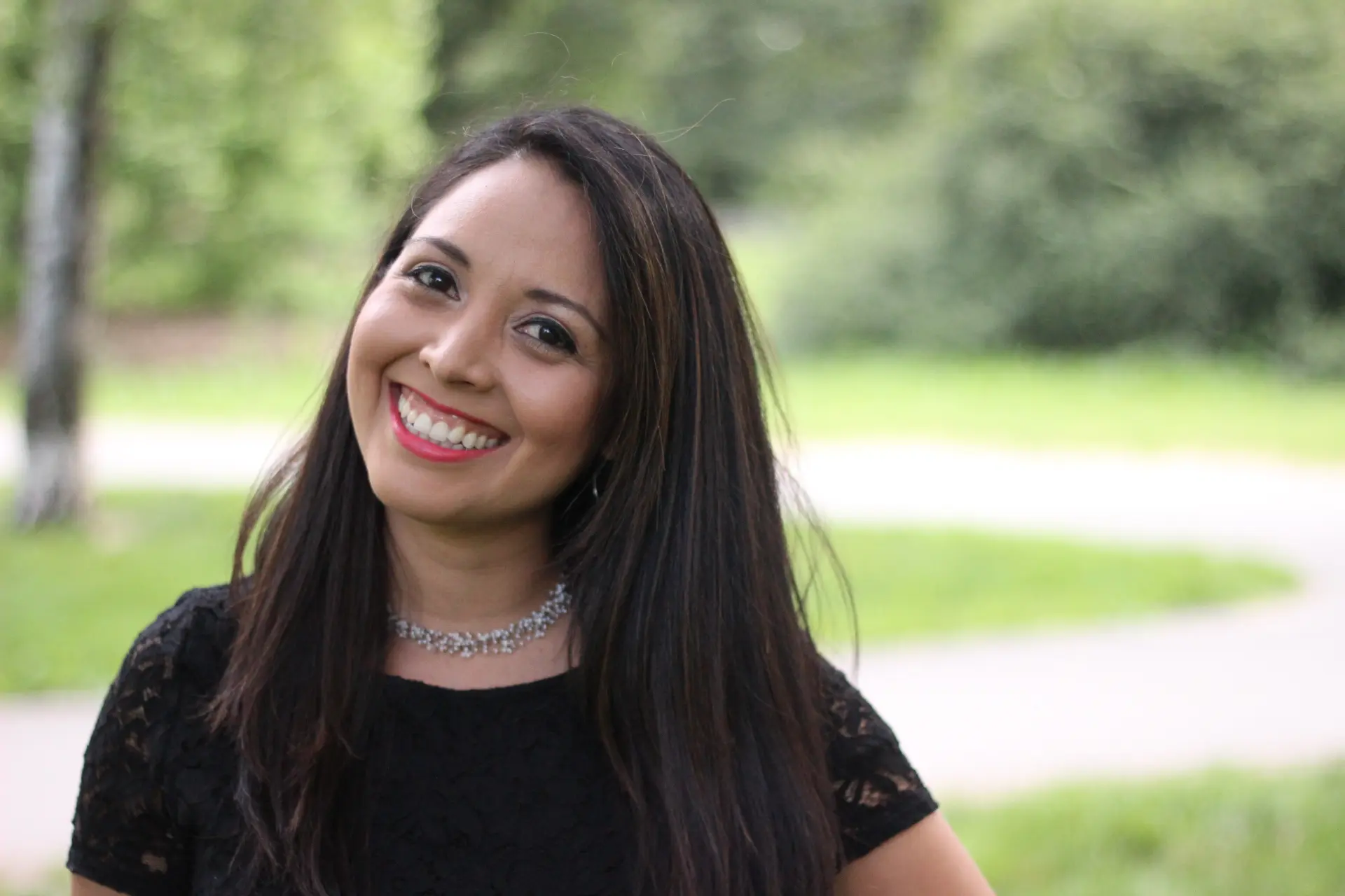 A woman smiling for the camera in front of some trees.