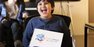 A boy sitting in a chair holding up an envelope.