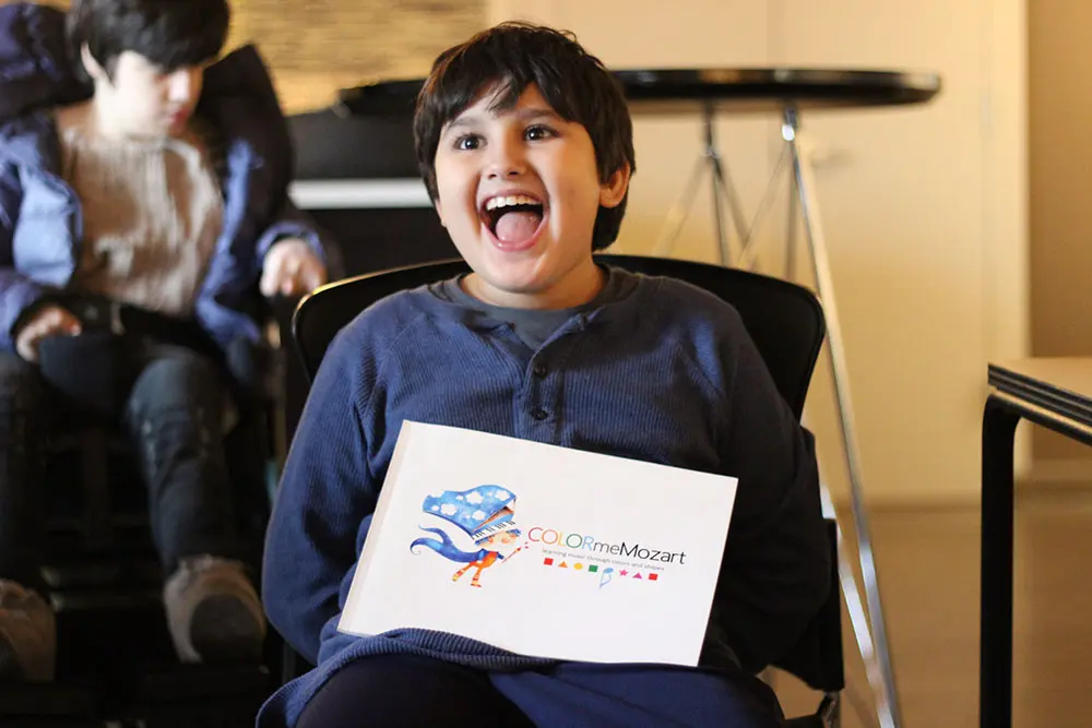 A boy sitting in a chair holding up an envelope.