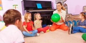 A woman holding a green ball in front of two children.