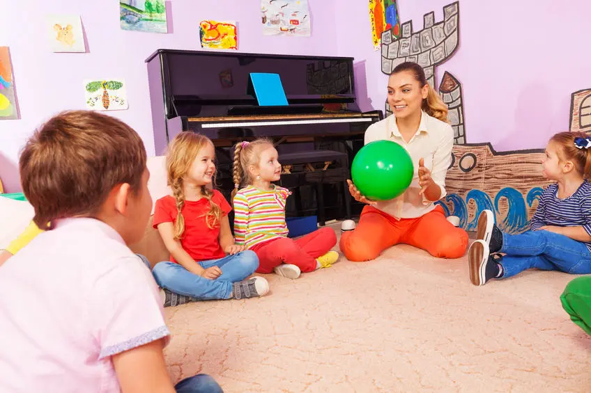 A woman holding a green ball in front of two children.