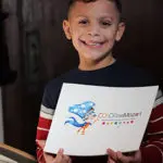 A boy holding up a drawing of a person.