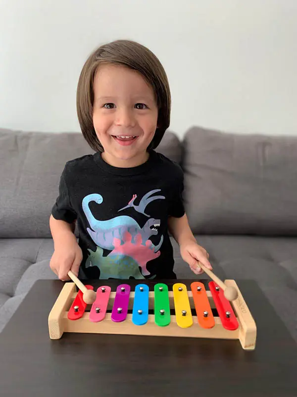 A little girl sitting on the couch playing with a toy xylophone.