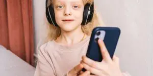 A girl with headphones on holding up her phone.