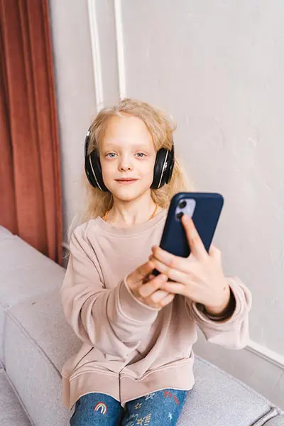 A girl with headphones on holding up her phone.