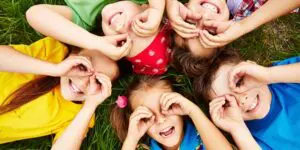 A group of children laying in the grass with their hands up.