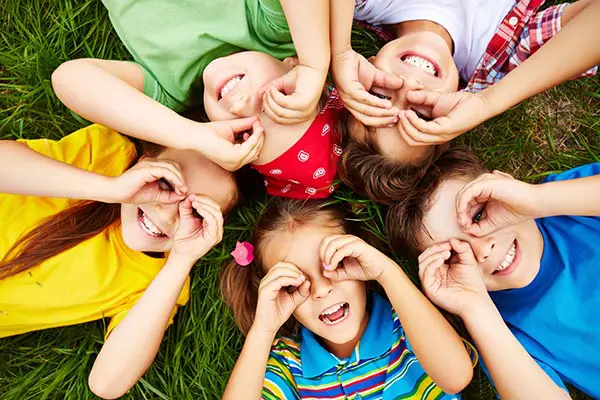 A group of children laying in the grass with their hands up.