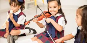 A group of children sitting on the floor playing violin.