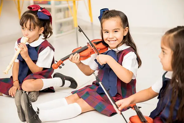 A group of children sitting on the floor playing violin.