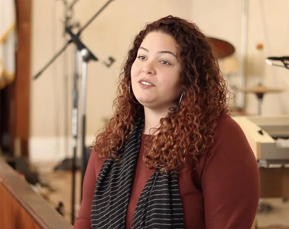 A woman with curly hair standing in front of a piano.