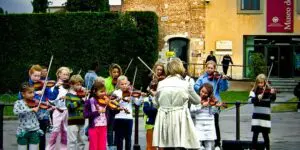 A group of children playing violin on the street.