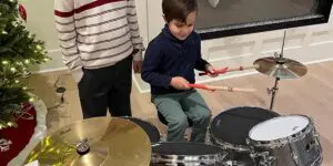 Two young boys playing drums in a living room.