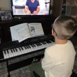 A boy sitting at the piano in front of a tv.