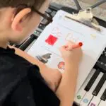 A young boy is writing on paper with a marker.