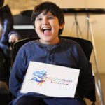 A boy sitting in a chair holding up a sign.