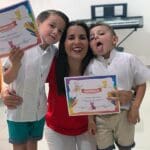 A woman holding two boys and one boy is smiling.