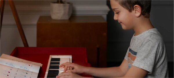 A young child playing the piano in front of a red chair.