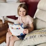 A girl sitting on the couch reading a book.