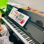 A child playing with an instrument on top of a piano.